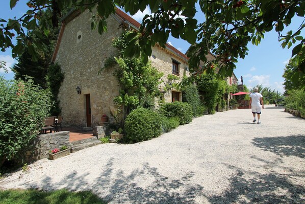 A stone building with a gravel driveway, surrounded by greenery and a red umbrella.
