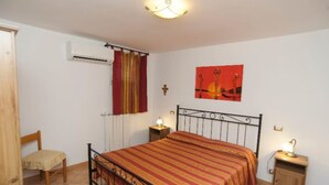 Camera da letto con un letto, una sedia, un comodino, condizionatore d'aria a muro, una finestra con tende e un quadro.