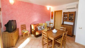Un accogliente soggiorno con un mobile TV in legno, un divano con una coperta colorata, un tavolo da pranzo con sedie e un angolo cucina con pensili in legno.