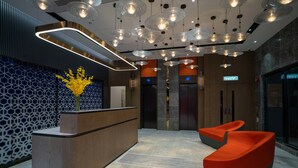 A modern reception area with a wooden reception desk, a vase of yellow flowers, and two orange chairs. - Le Hoteru (Kowloon)