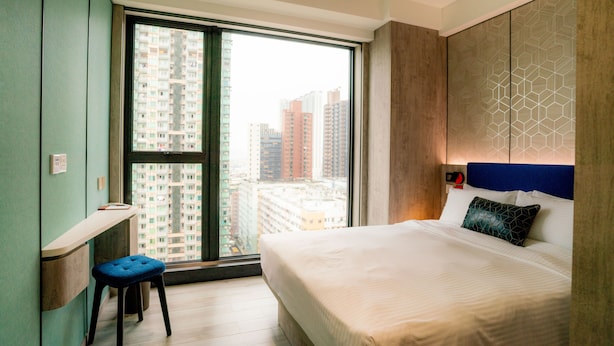 A modern hotel room with a large window, a bed with a geometric-patterned headboard, and a small desk with a chair. - Le Hoteru (Kowloon)
