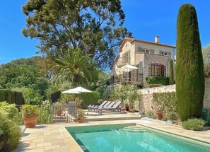 A stone building with a pool, surrounded by greenery and a clear sky.