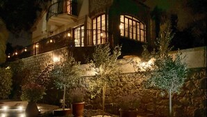 A stone building with multiple windows and balconies, illuminated by warm lighting. - LUXURY 3 BED VILLA with AMAZING VIEW and PRIVATE HEATED POOL in GORGEOUS GARDENS (Mougins)