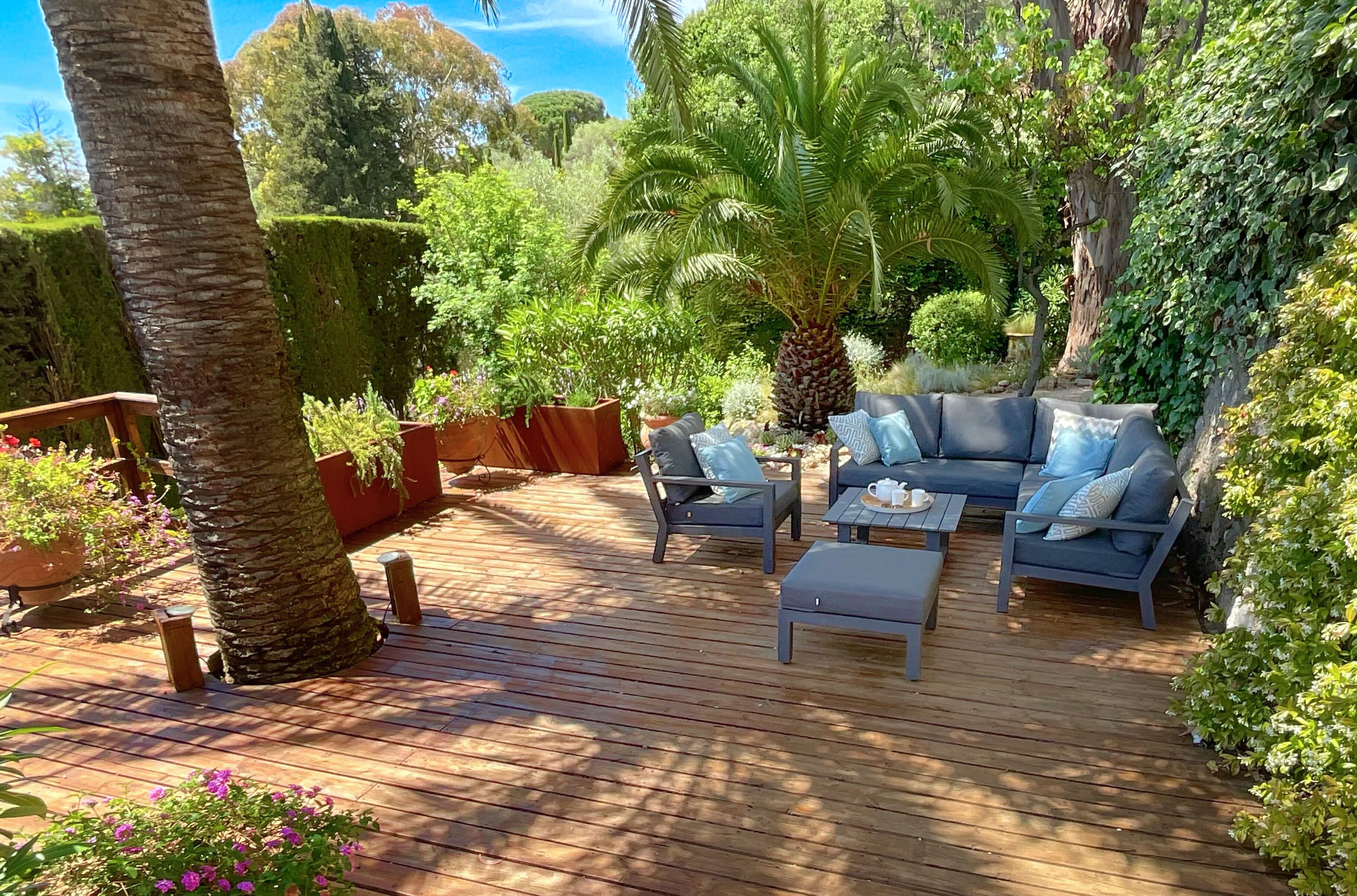 Terraza de madera con mobiliario exterior, rodeada de abundante vegetación y árboles.