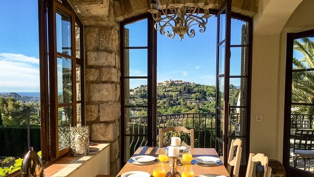 A breakfast table set with plates, glasses, and a fruit plate, overlooking a scenic landscape with stone walls and a view of a hill. - LUXURY 3 BED VILLA with AMAZING VIEW and PRIVATE HEATED POOL in GORGEOUS GARDENS (Mougins)