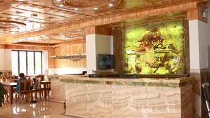 Zona de recepción de hotel con mostrador de mármol, techo de madera y un gran elemento decorativo en la pared.