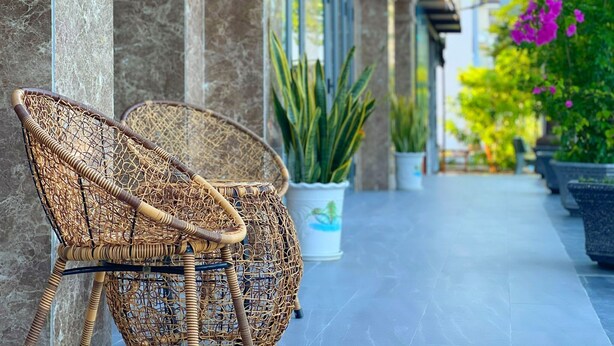 Una silla de mimbre y plantas en macetas en un patio con baldosas.