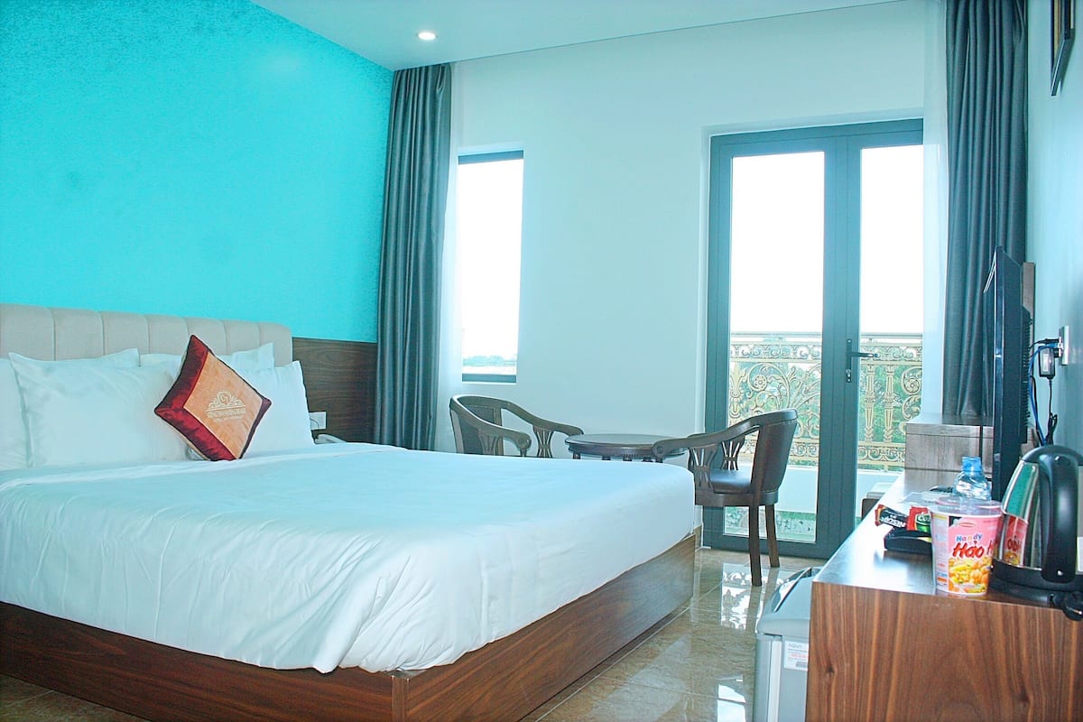 Une chambre d’hôtel avec un grand lit, un bureau avec une chaise, une télévision et un balcon avec vue.