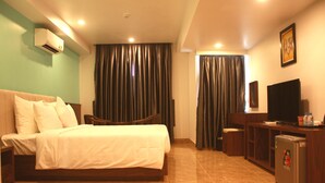 Habitación de hotel con cama, escritorio con computadora, televisor y aire acondicionado.