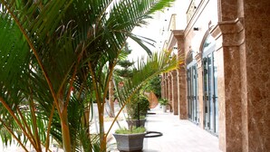 Un pasillo con palmeras, plantas en macetas y piso de mármol.