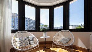 Ein Eckzimmer mit zwei weißen Korbstühlen, einem kleinen weißen Tisch und einer Topfpflanze.