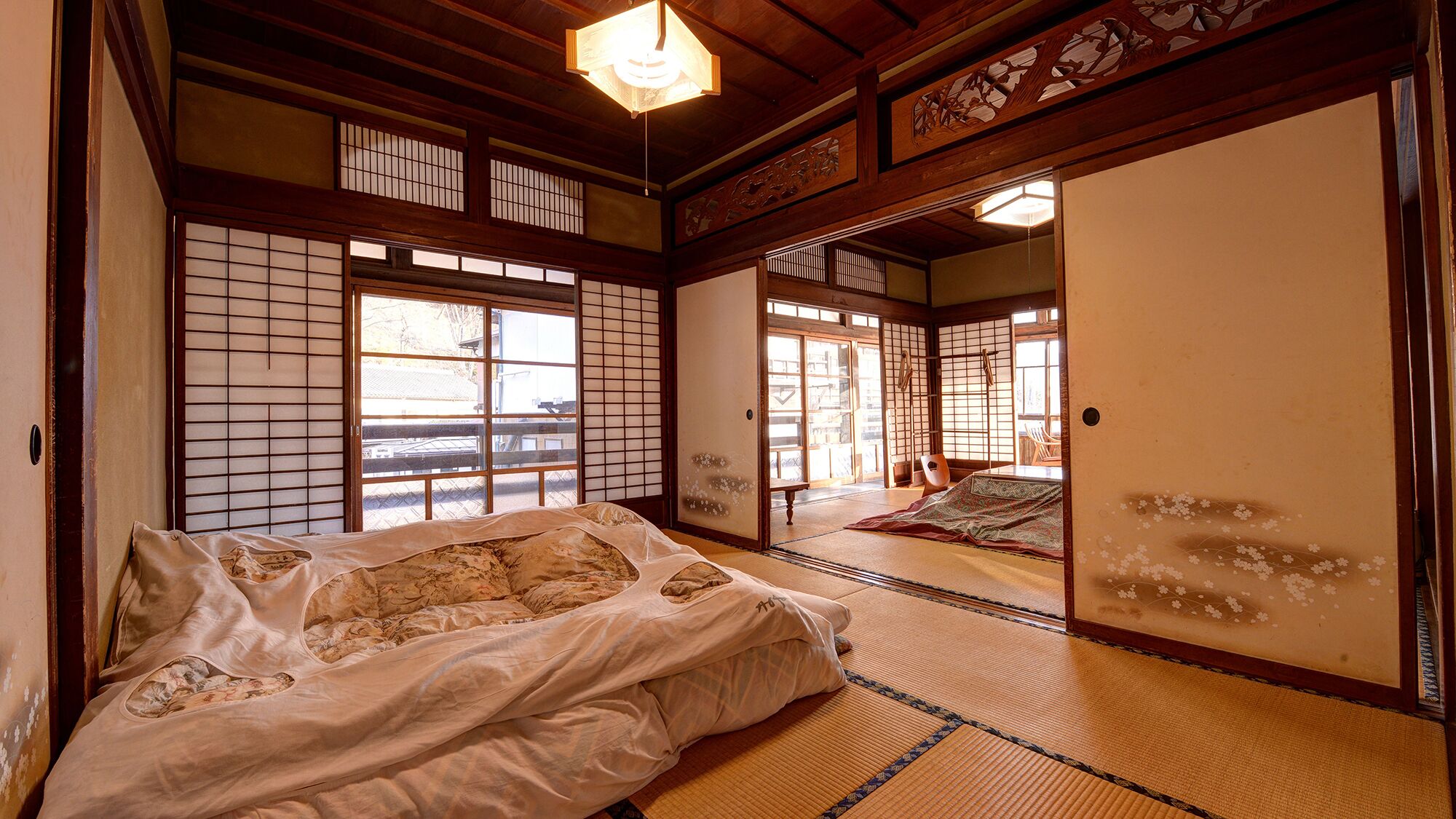 Una habitación japonesa tradicional con suelo de tatami, futón, puertas correderas y vistas al exterior.