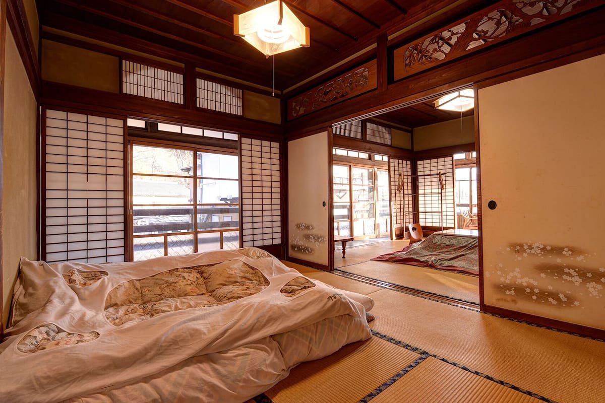 Perinteinen japanilainen huone, jossa on tatamimatto, futon-patja, liukuovet ja näkymä ulos.