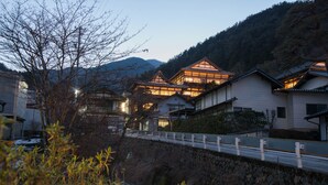 Ein traditionelles japanisches Gebäude mit mehreren Holzbauten, einer Stegbrücke und einer Bergkulisse.