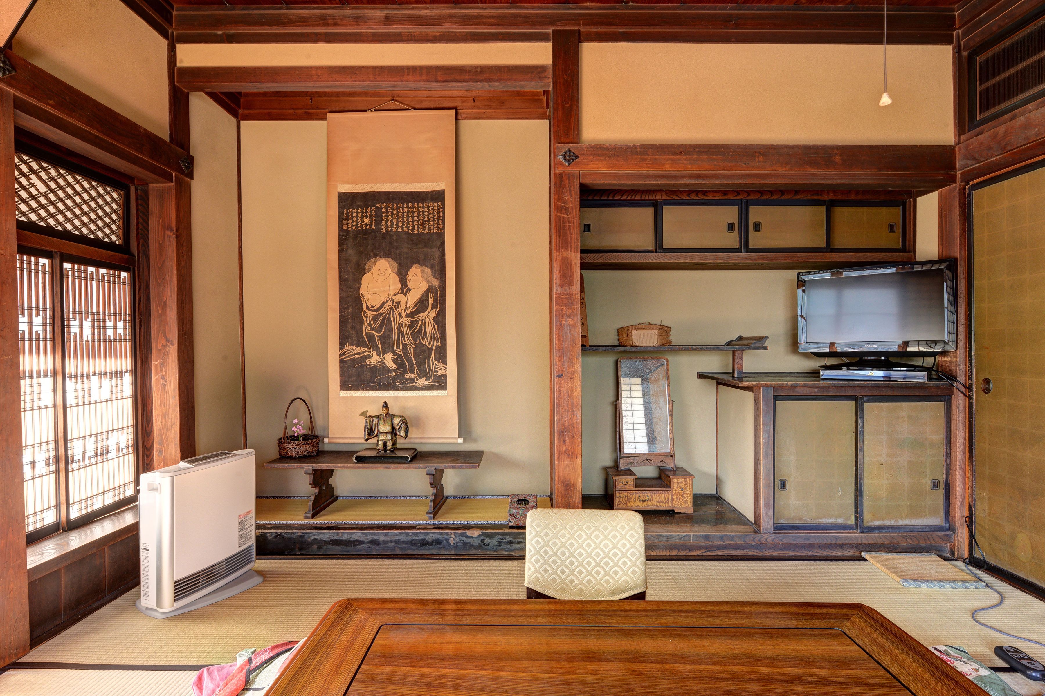 Una habitación japonesa tradicional con suelo de tatami, un rincón de asientos sobre tatami, un televisor en un mueble de madera y una puerta corredera.