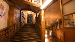 Eine Holztretreppe in einem Gebäude mit Holzwand und -geländer, die zu einer oberen Ebene führt.