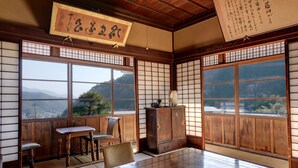 Ein traditioneller japanischer Raum mit Tatami-Boden, einem niedrigen Holztisch und Blick auf Berge durch große Fenster.