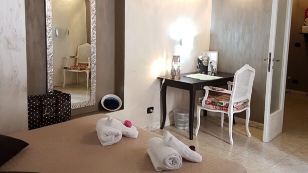 A hotel room with a bed, a desk, a chair, a mirror, and a door.