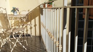 A balcony with a metal table and chairs, a potted plant, and a white railing.