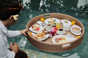 A wicker dining set with plates, cups, and food items by a poolside. - Moringa Ubud Villa (Ubud)
