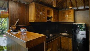 A kitchen with wooden cabinets, a black countertop, and a refrigerator with floral design. - Moringa Ubud Villa (Ubud)