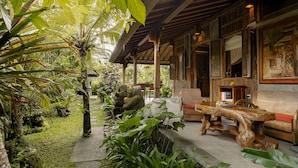 A wooden veranda with a stone pathway, surrounded by lush tropical plants and a palm tree. - Moringa Ubud Villa (Ubud)
