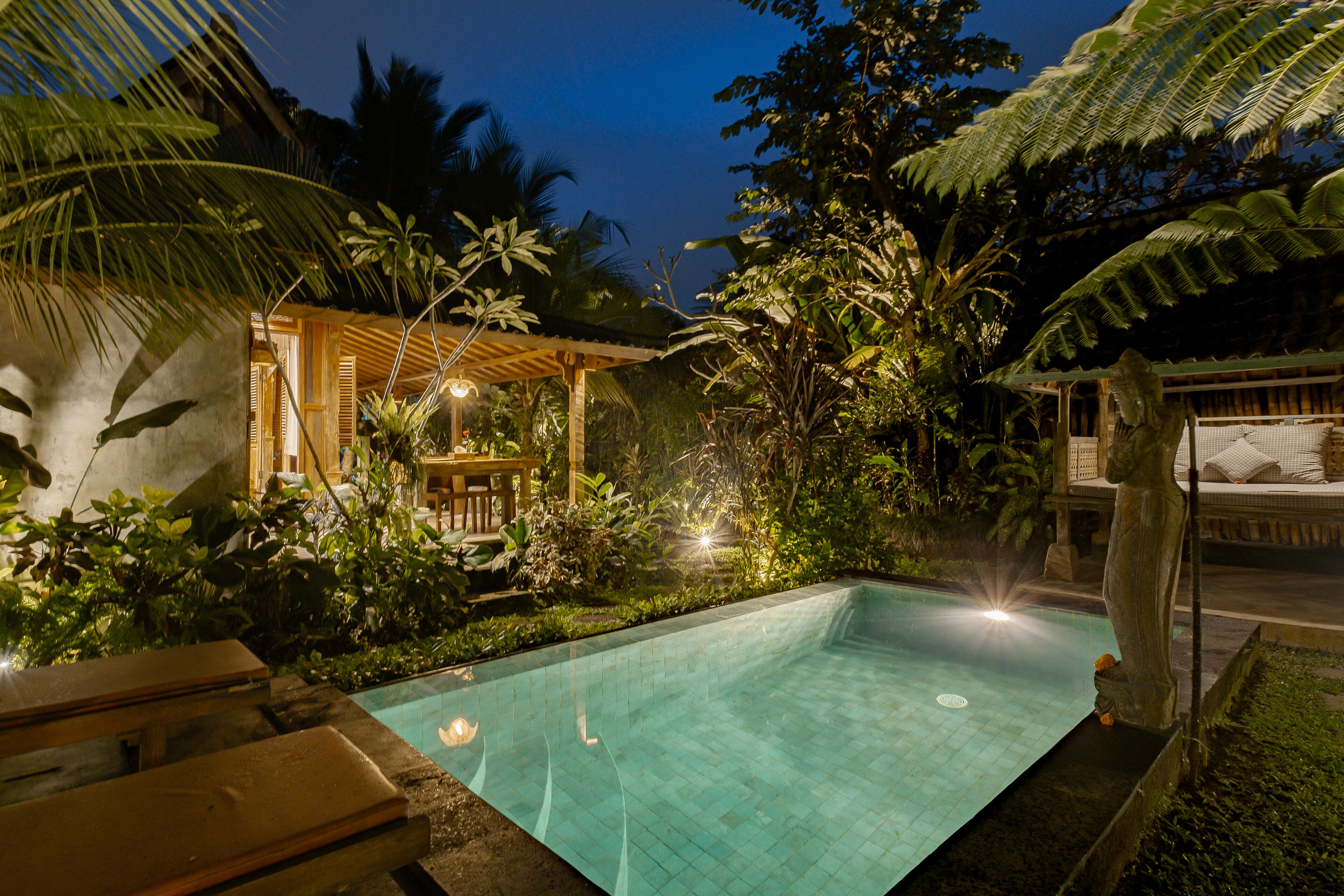 A rectangular swimming pool surrounded by lush tropical vegetation and wooden structures.