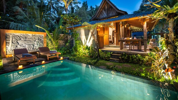 A poolside area with lounge chairs, a covered seating area, and a stone wall with carvings. - Moringa Ubud Villa (Ubud)