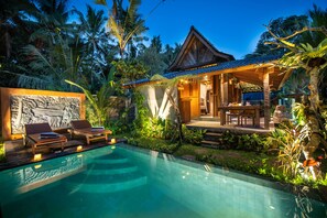 A poolside area with lounge chairs, a covered seating area, and a stone wall with carvings. - Moringa Ubud Villa (Ubud)