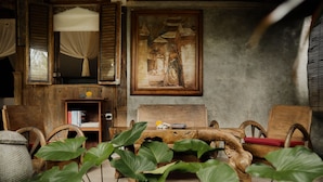 A rustic room with a wooden bench, a painting on the wall, and a mirror with curtains. - Moringa Ubud Villa (Ubud)