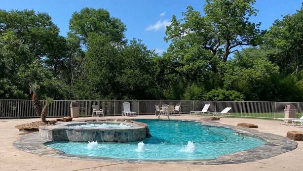 A hot tub surrounded by a pool, with lounge chairs and a fence. - Guadalupe Dew Drop Inn |Pools | Monthly Discounts (New Braunfels)