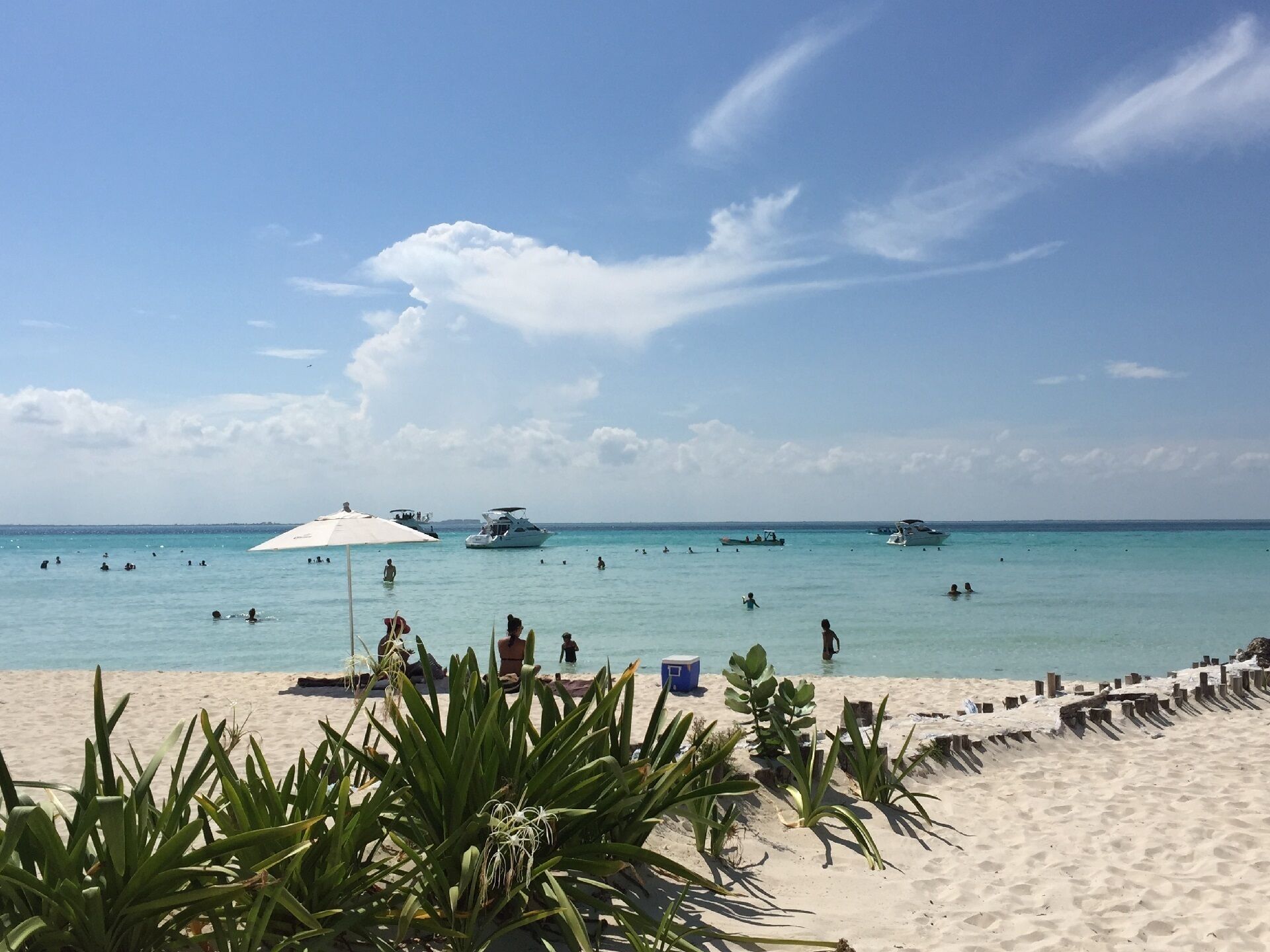 A beach with clear turquoise water, several boats, and people swimming.