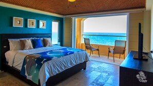 Ein Schlafzimmer mit Bett, Deckenventilator und Blick auf das Meer durch eine offene Tür.