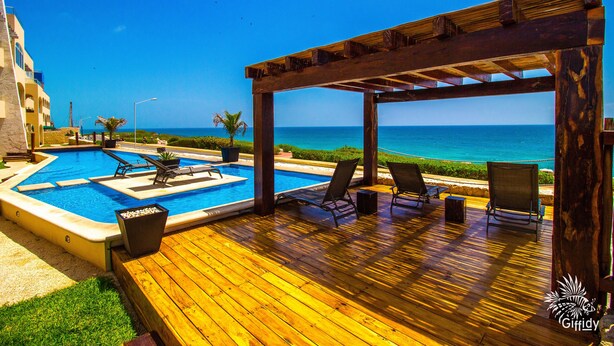 Eine Holzterrasse mit Pool, Liegestühlen und Blick auf den Ozean.