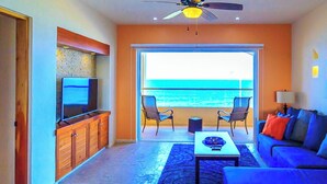 Ein Wohnzimmer mit einer Couch, Sesseln, einem Fernseher und Meerblick.