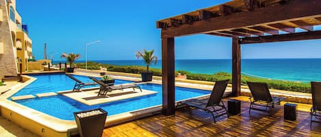 A wooden deck with a pool, lounge chairs, and a view of the ocean.