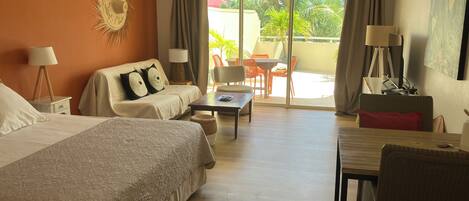 A hotel room with two beds, a sofa, a dining table, and a balcony with outdoor furniture.
