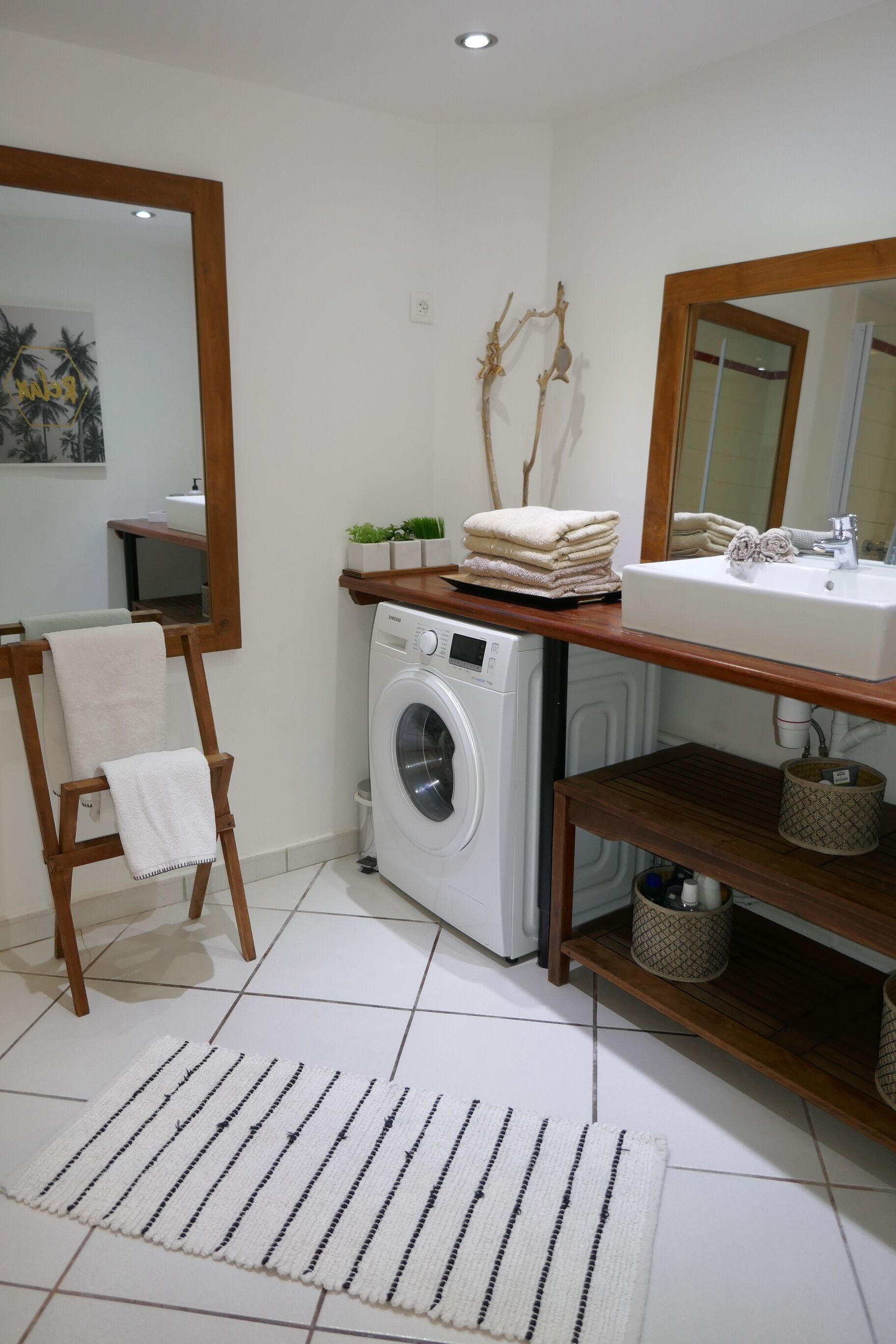 Une petite salle de bain équipée d’un lave-linge, d’un lavabo, d’un miroir et d’un porte-serviettes.