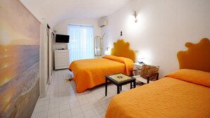 Ein Hotelzimmer mit zwei Betten, einem Fernseher, einem Schminktisch, einem Fenster mit Vorhängen und einem an der Wand befestigten Spiegel.