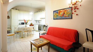 Ein Wohnzimmer mit einem roten Sofa, einem Couchtisch mit einem Bild, einem Essbereich mit Tisch und Stühlen und einer Küche im Hintergrund.