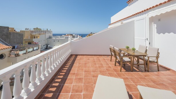 Un balcon doté d’un sol carrelé, d’une balustrade blanche et d’une table avec des chaises.