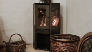 A wood-burning stove with visible flames, a woven basket, and a metal tool on the floor.