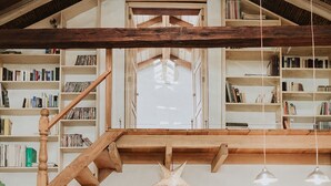 A spacious loft with a wooden staircase, a reading nook, and a large window.