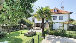 A backyard with a swimming pool, a barbecue area, and a white house with a red-tiled roof.