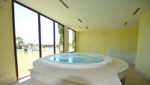 A room with a hot tub, large windows, and a view of a pool and greenery. - Parque Botanico Holiday Rentals (Benahavis)