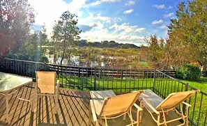A deck with a table and four chairs, overlooking a body of water and a grassy area with trees. - Spacious, open, home on a nature preserve/wetland, with Golf Cart! (The Villages)