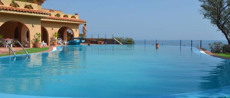A swimming pool with a view of the ocean, a building with arches, and a palm tree.