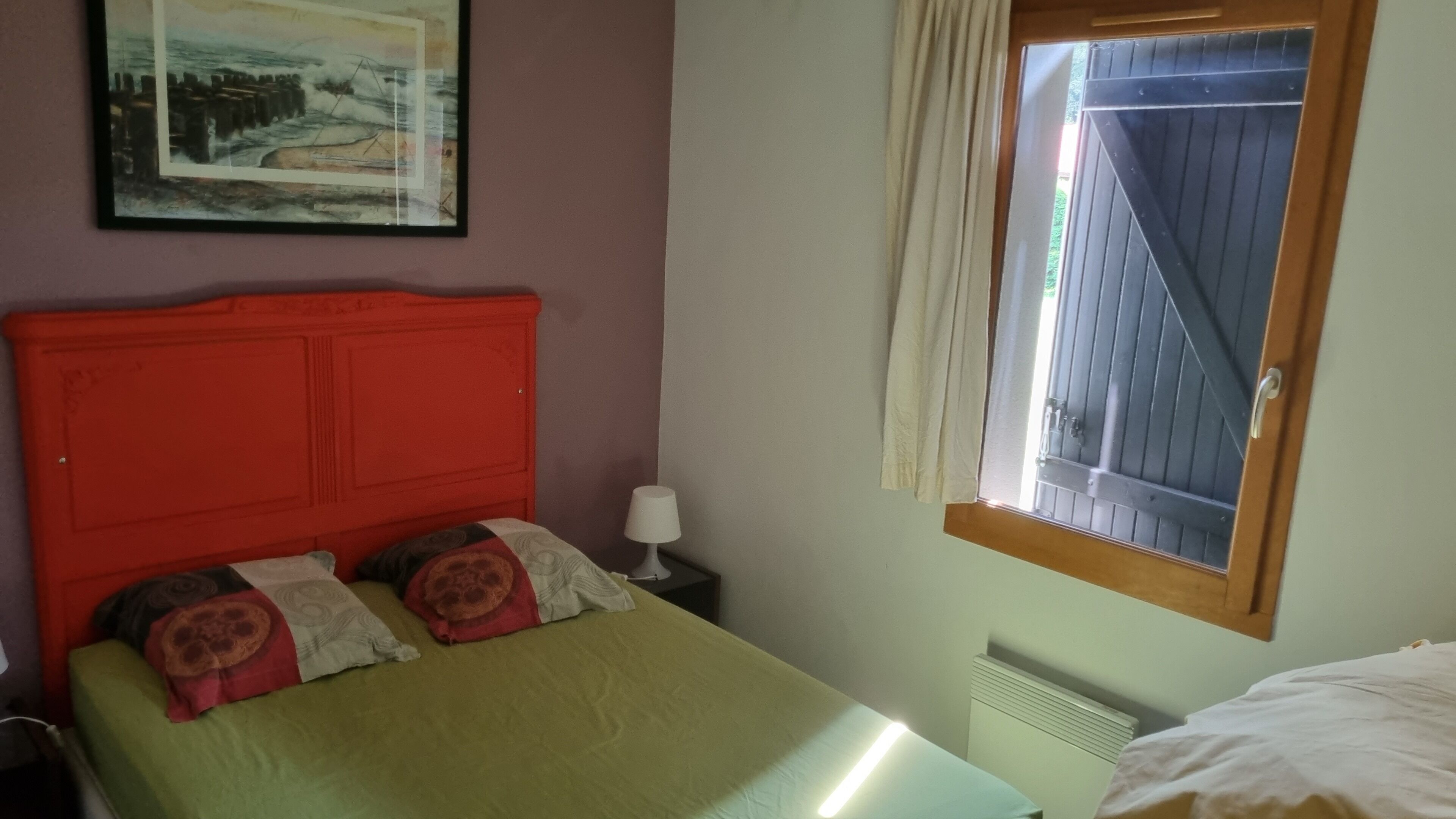 A bed with a red headboard, a bedside lamp, and a window with curtains.