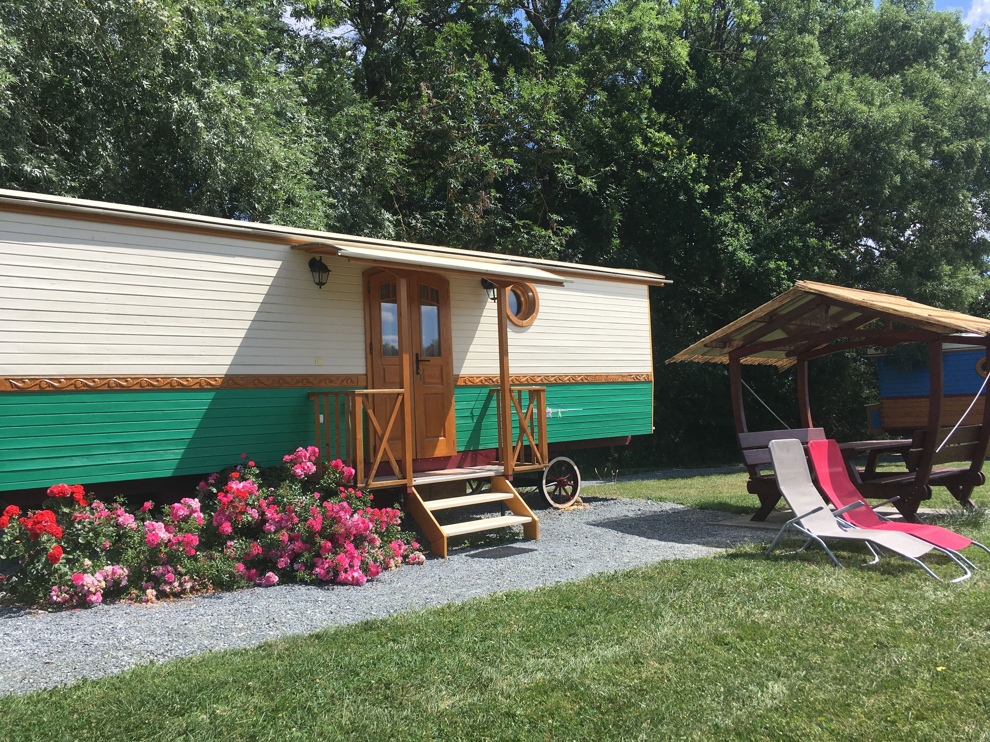 En campingvogn med veranda, et lille tilbygget rum og et picnicbord med liggestole.