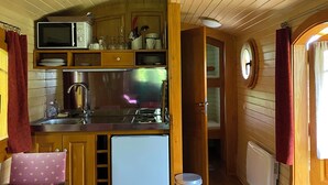 Een kleine keuken met houten kastjes, een magnetron, een koelkast en een spoelbak.